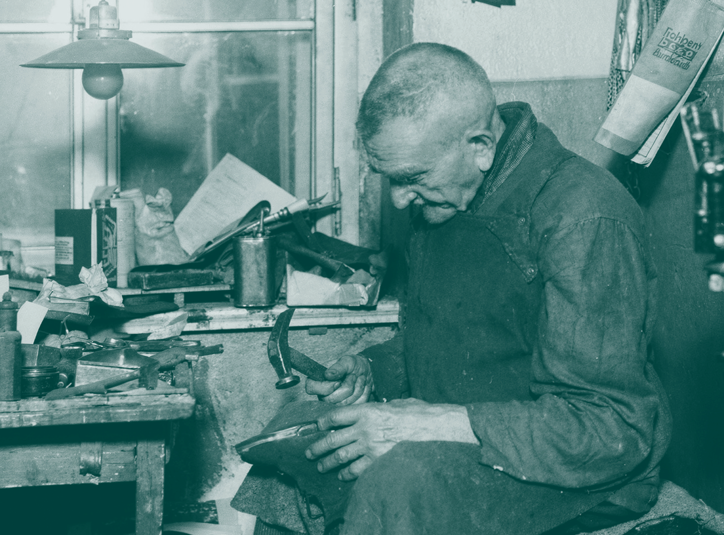 Alter Schuhmacher in kleiner Werkstatt bearbeitet einen Schuh mit einem Hammer